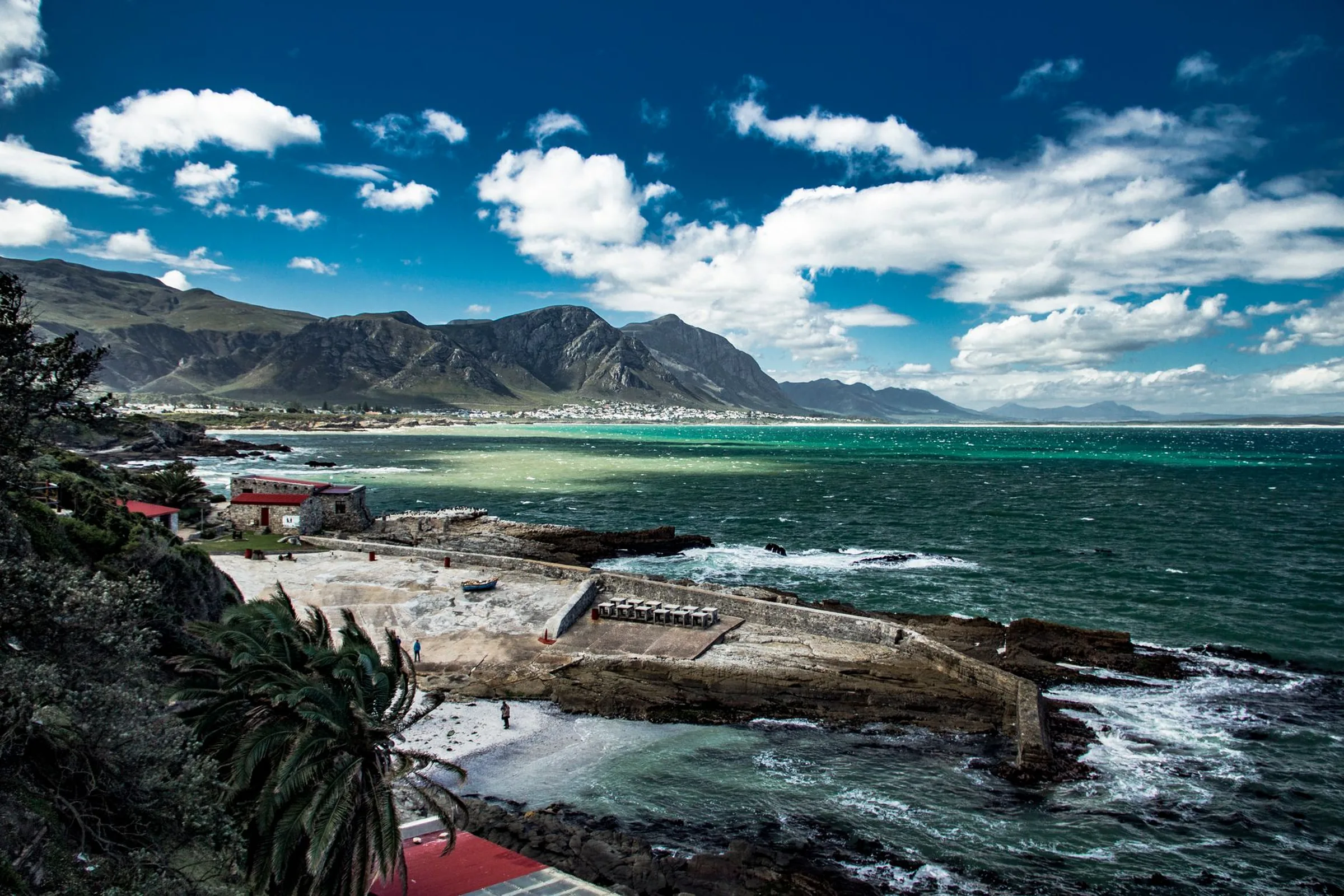 A stone harbour wall and slipway on a rocky shore, with a long bay and mountains behind