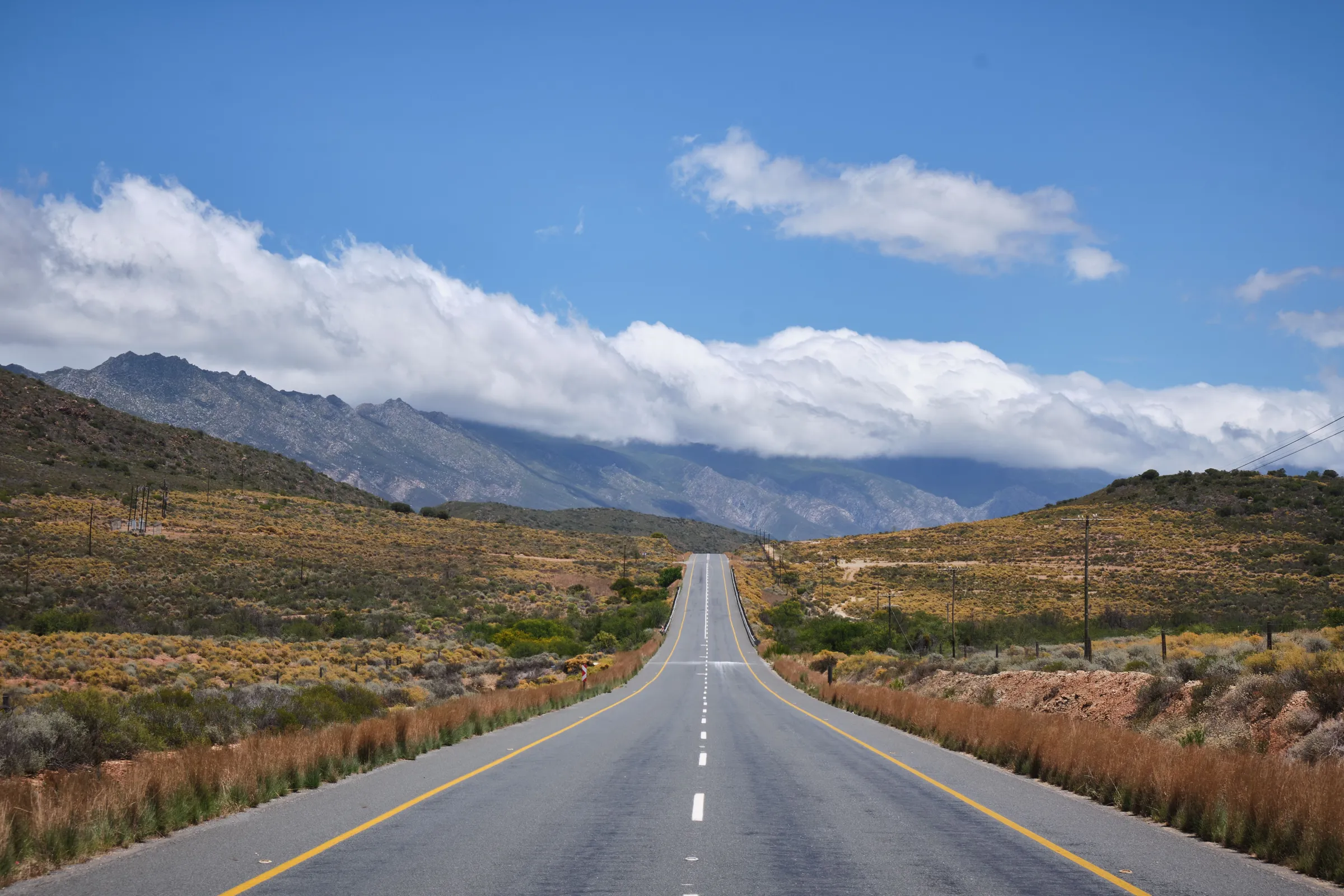 A two-lane road running between grassy hills under white clouds
